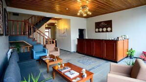 A spacious living area with a wooden ceiling, a reception desk, a staircase, and a reception sign. - Ahıska Palas (Kars)