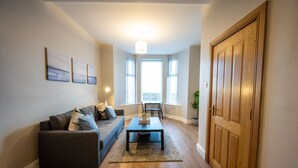 A living room with a sofa, coffee table, and a wooden door. - Apartment - Ground Floor (Newcastle)