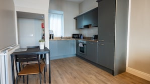A modern kitchen with a dining table, chairs, a microwave, an oven, and a refrigerator. - Apartment - Ground Floor (Newcastle)