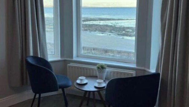 A corner room with a large window overlooking the sea, two chairs, a small table with a plant, and a radiator. - Apartment - Ground Floor (Newcastle)