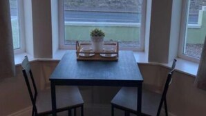 A dining area with a table and chairs, a potted plant, and a view of the sea through large windows. - Apartment - Ground Floor (Newcastle)