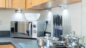 A kitchen with wooden cabinets, a microwave, a gas stove, and a knife block. - Apartment 8 (Worksop)
