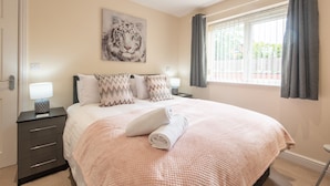 A bedroom with a large bed, a nightstand with a lamp, a painting of a tiger on the wall, and a window with curtains. - Apartment 8 (Worksop)