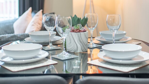 A dining table set with white plates, glasses, and a centerpiece with a plant and a vase. - Apartment 8 (Worksop)