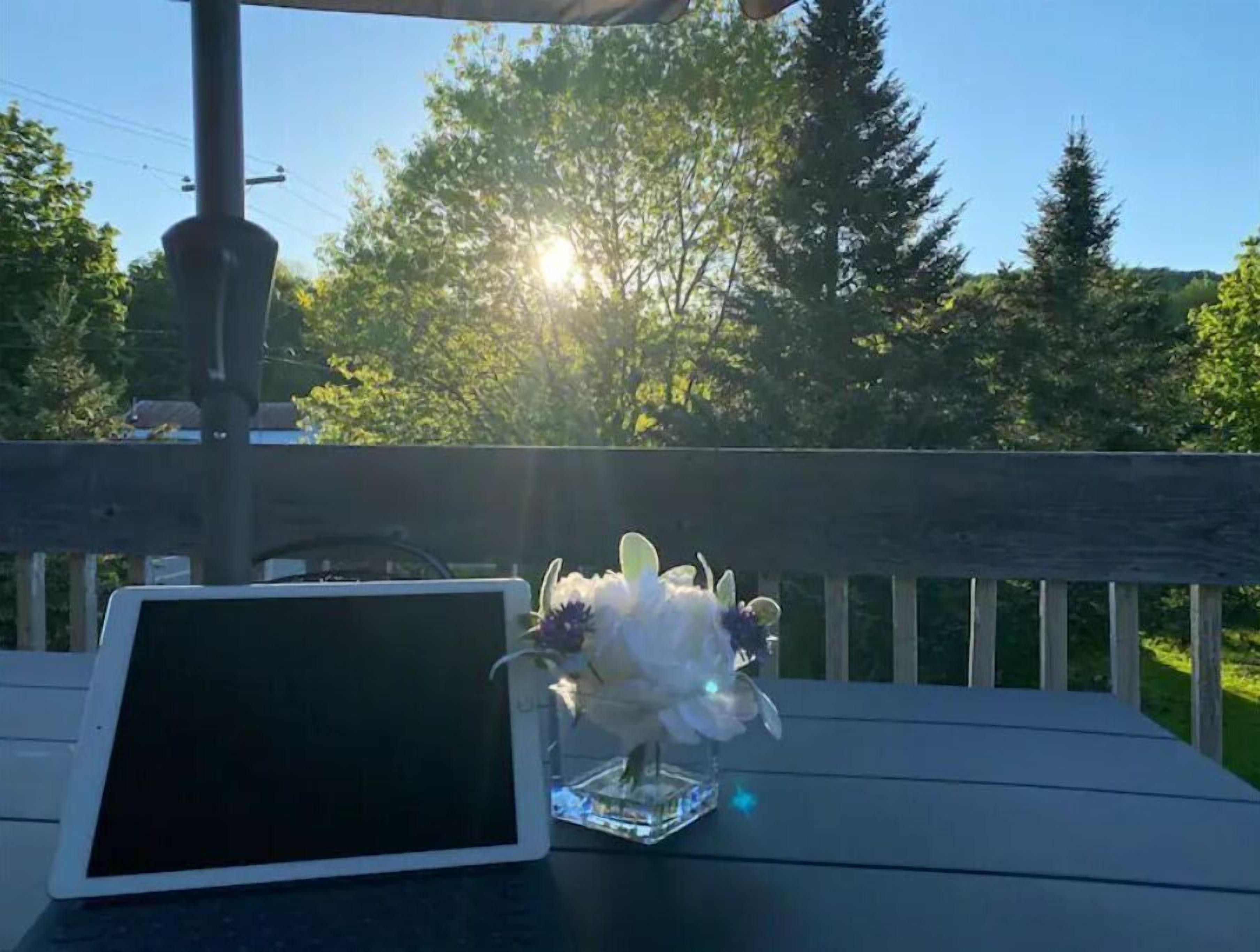 Una tableta sobre una terraza de madera, con un florero de vidrio con flores.