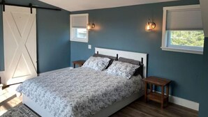 Une chambre à coucher comprenant un lit, deux tables de chevet, une fenêtre avec des stores et une porte ornée d’un motif en forme de croix.