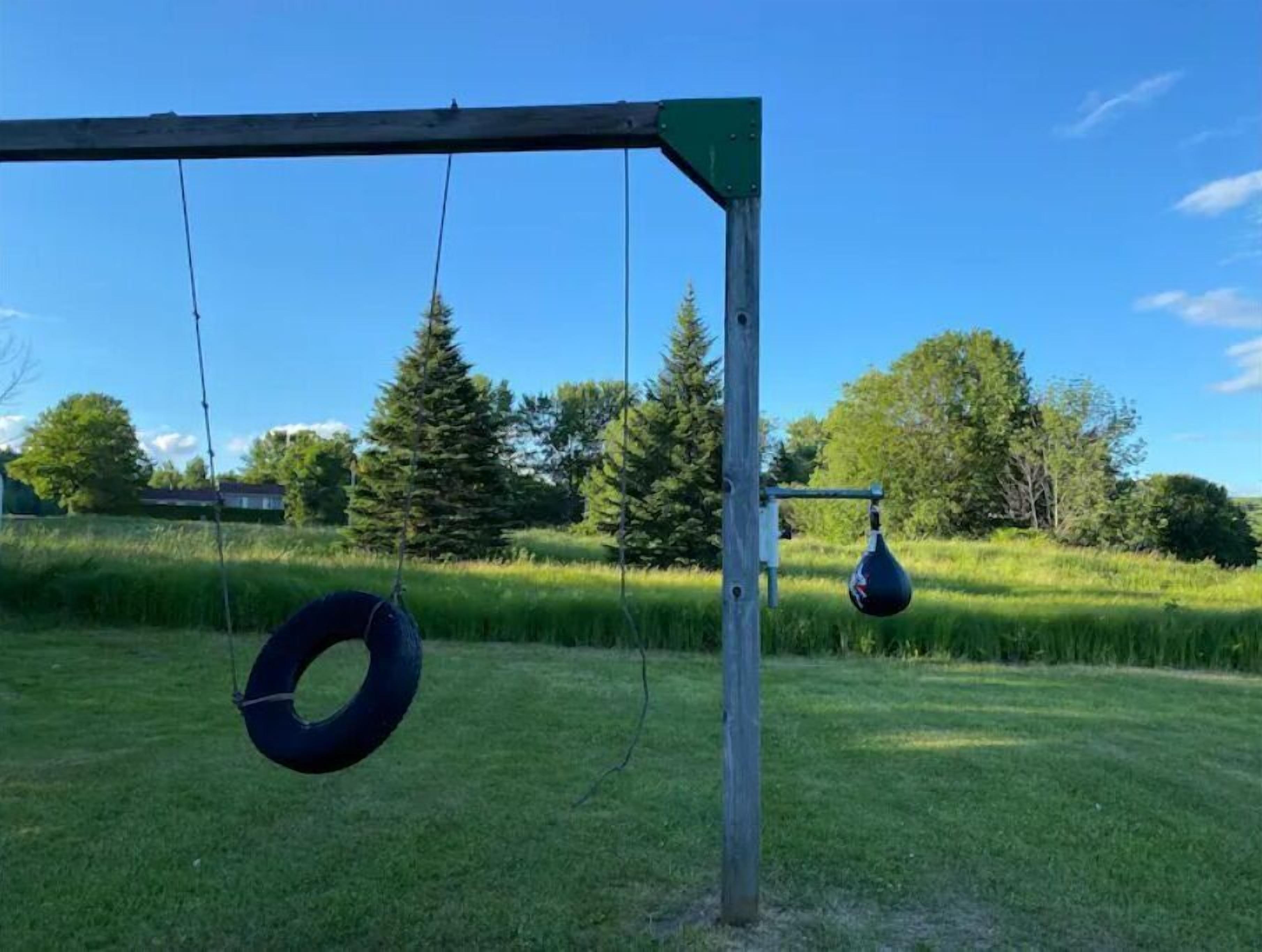A playground with a swing set and tire swings in a grassy field with trees and houses in the background.