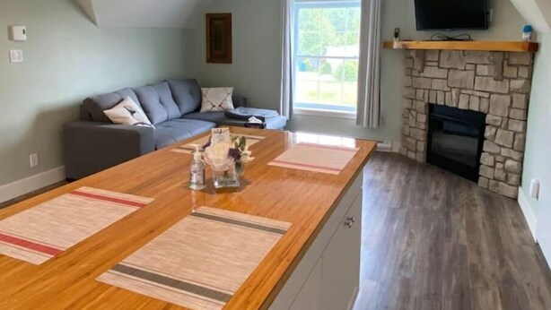 Un salon moderne avec une table à manger en bois, un canapé gris, une cheminée en pierre et un téléviseur fixé au mur.