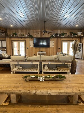 A spacious living room with a large sofa, wooden ceiling, and a flat-screen TV mounted on the wall. - Peaceful Retreat! Cozy Lodge with Scenic Views, Patio, Fire Pit. (Pinopolis)