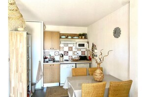 Une cuisine compacte dotée de meubles en bois, d’un four à micro-ondes et d’un coin repas avec des chaises et une table en osier.