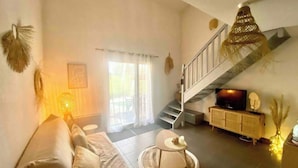 A living room with a sofa, a coffee table, a TV, and a staircase. - Fully-equipped bastidon in the heart of the Ventoux (Aubignan)