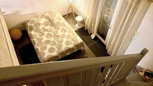A bedroom with a bed, a small bedside table, a lamp, a toilet, and a window with curtains. - Fully-equipped bastidon in the heart of the Ventoux (Aubignan)