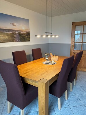Ein Esstisch mit sechs Stühlen, ein Holzboden, ein an der Wand hängendes Bild und eine Tür mit Glasfenster.