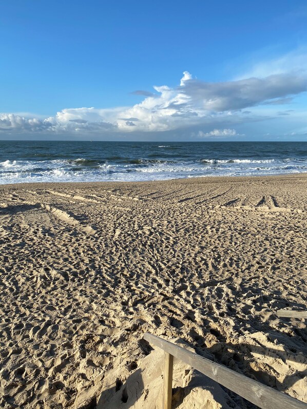 A sandy beach with a wooden fence in the foreground and the ocean in the background.