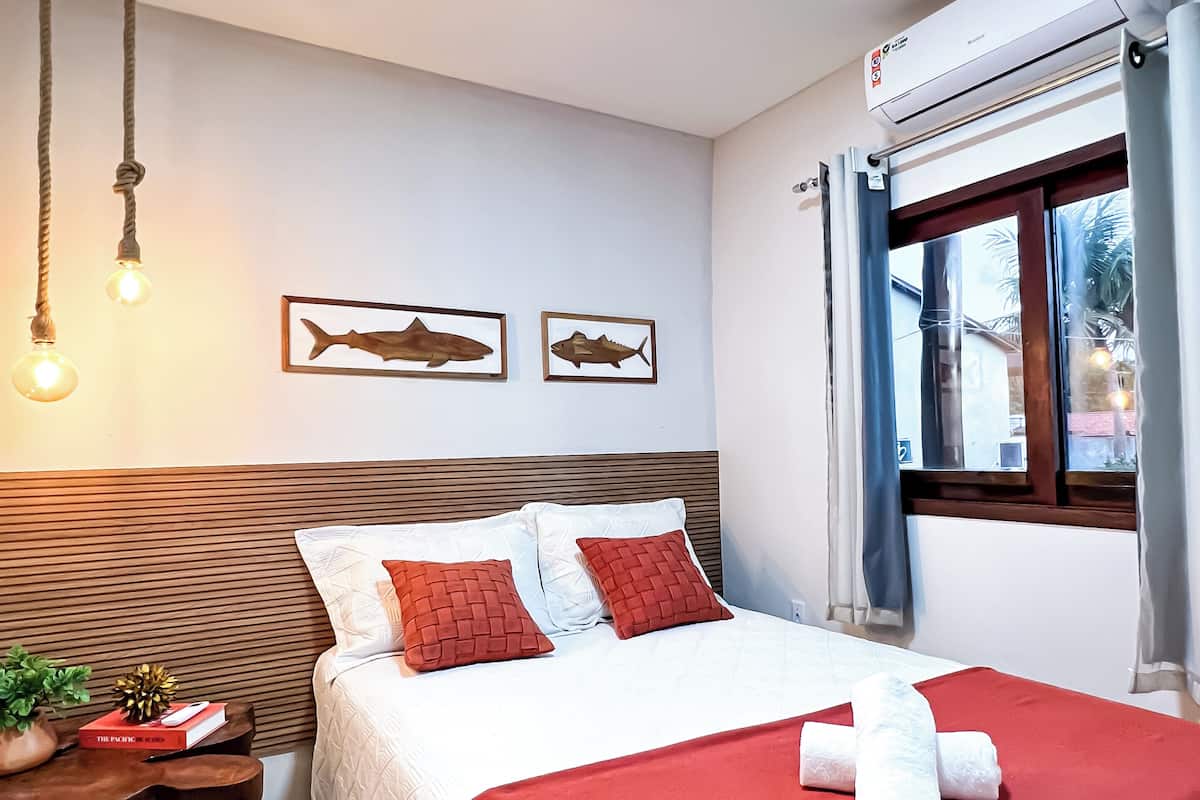 A neatly arranged bedroom with a bed, pillows, a bedside table with a plant, and a window with curtains.