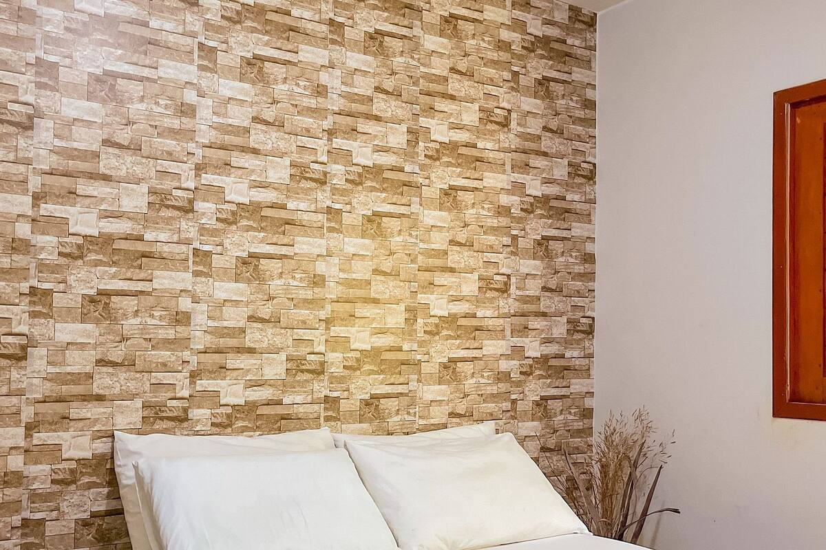 A bedroom with a stone-patterned headboard, a bed with white linens, and a wooden nightstand.