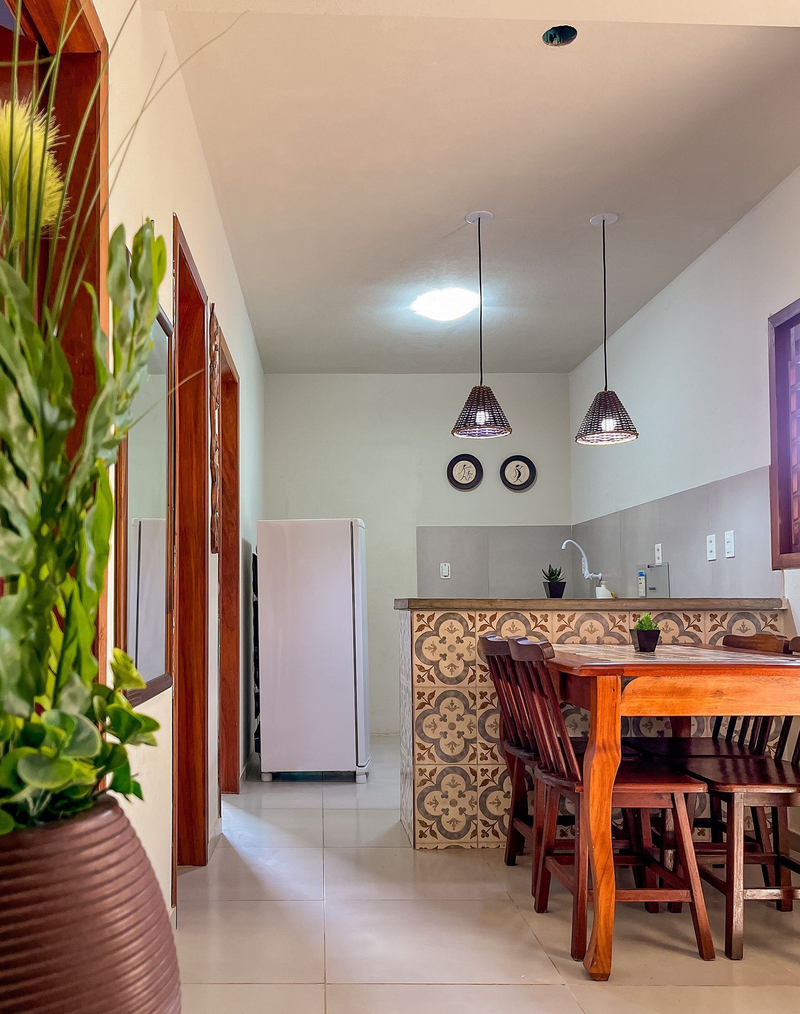 A kitchen with a dining area, featuring a refrigerator, pendant lights, and a tiled backsplash.