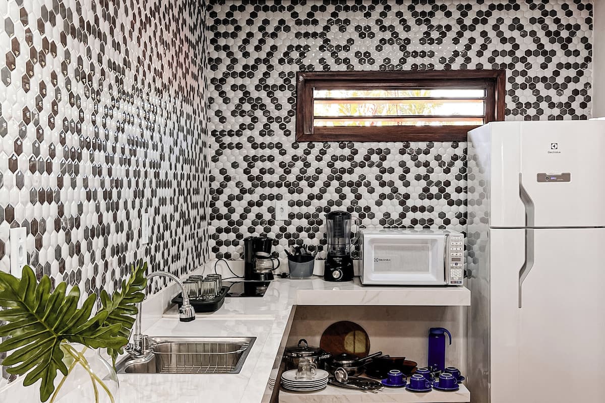 A kitchen with a patterned backsplash, a window, a refrigerator, and a countertop with various appliances and items.