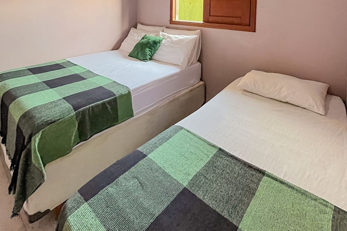 A room with two beds, each with a green and black checkered bedspread, a wooden door, and an air conditioning unit on the wall.