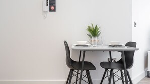 A modern dining area with a white table, two black chairs, a small potted plant, and a wall-mounted phone. - Seven Living Solihull - Broadoaks Studio (Solihull)