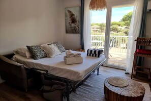 A bedroom with a bed, a chair, a small round table, and a balcony with a railing.
