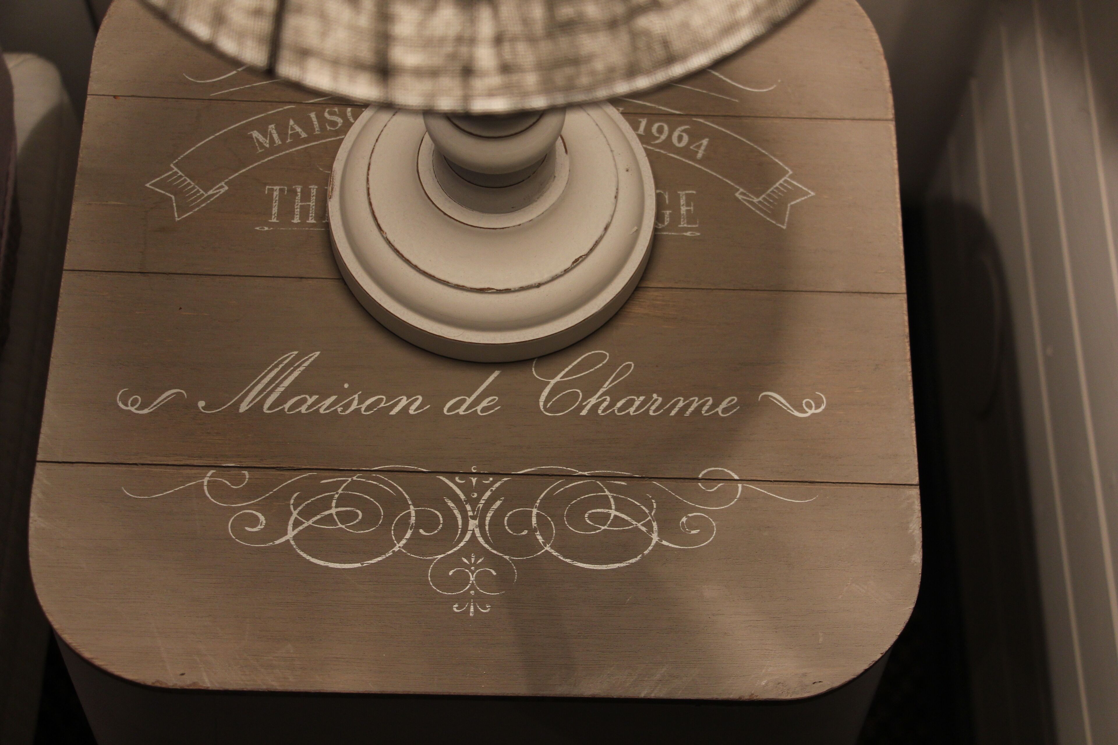 A wooden table with a lamp on top, featuring decorative text and a floral design.