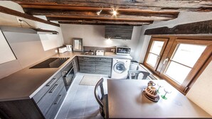 A compact kitchen with a built-in oven, a washing machine, and a dining area with a table and chairs. - Cottage 'BRAND (Turckheim)