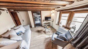 A cozy living room with a sofa, a coffee table, and a TV. There's a wooden ceiling and a window with curtains. - Cottage 'BRAND (Turckheim)