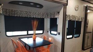 Ein kleiner Essbereich mit einem Tisch und orangefarbenen Stühlen, einer Vase mit Ästen und einem Fenster mit einem gemusterten Vorhang.