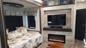 Ein Schlafzimmer mit einem Bett, einem Fernseher, einem Kamin und einem Laptop auf einem Holztisch.