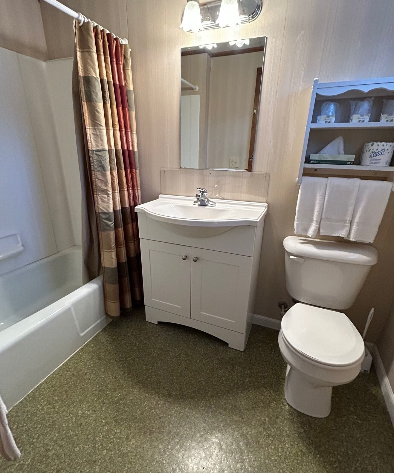 A bathroom with a white sink, mirror, and toilet. There is a shower curtain and a shelf with towels.
