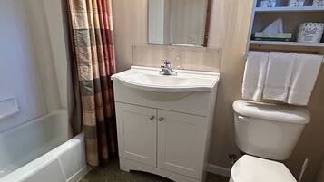 A bathroom with a white sink, mirror, and toilet. There is a shower curtain and a shelf with towels.
