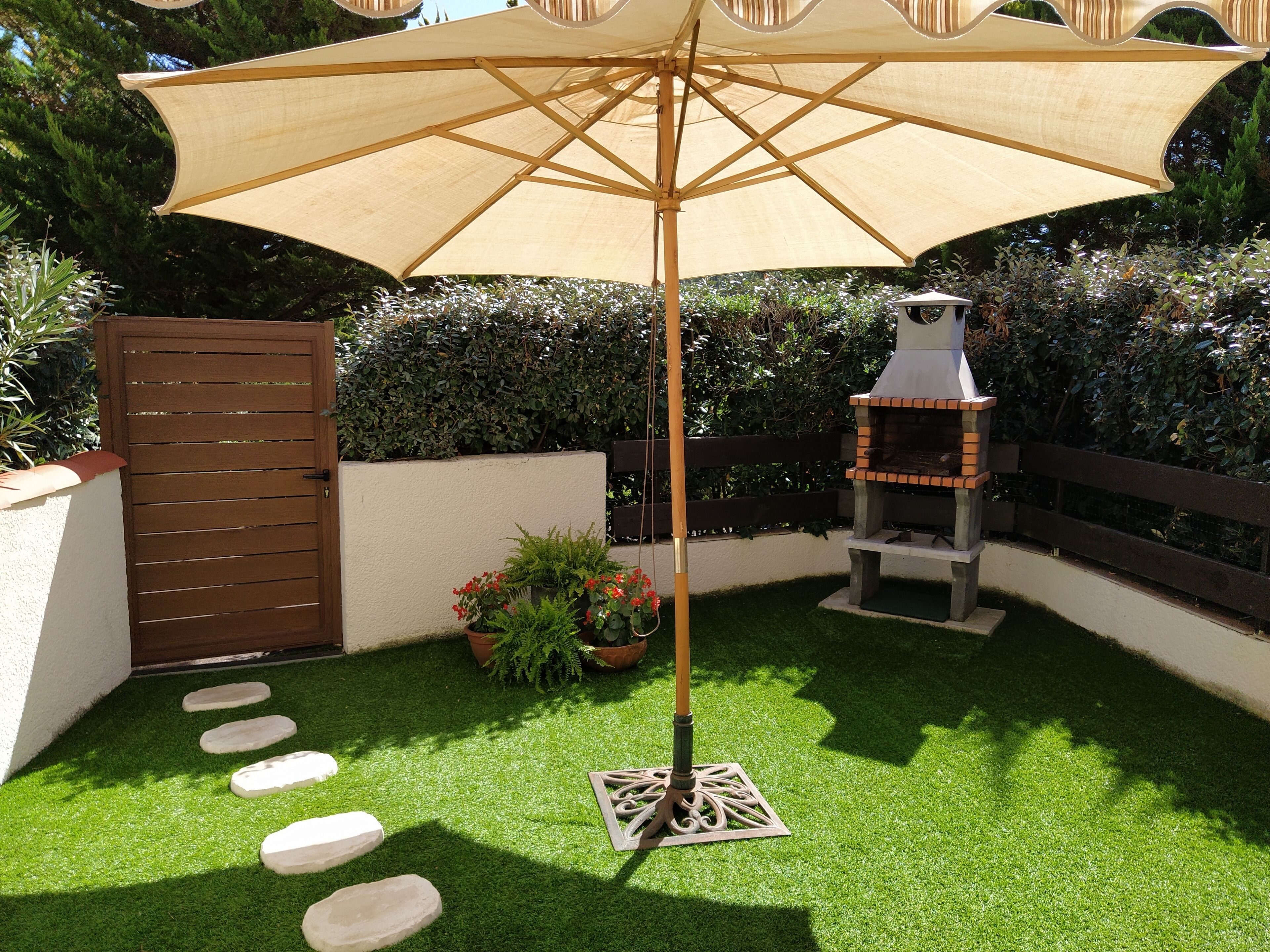 Un patio con cerramiento de madera, una parrilla, una planta en maceta y un sendero de adoquines.
