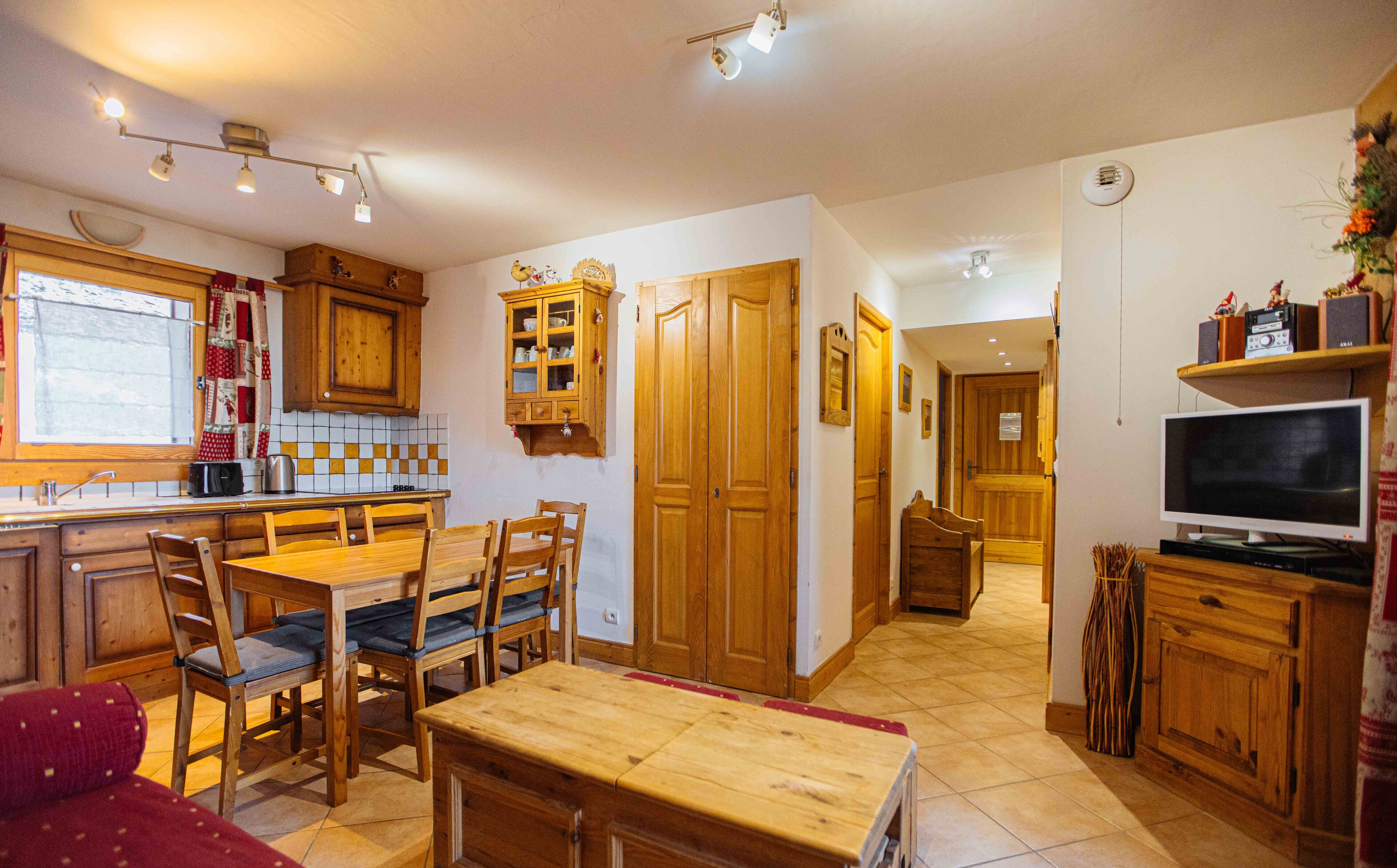 A cozy kitchen with wooden cabinets, a dining area with a table and chairs, and a television on a wooden stand.