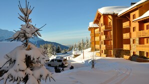 Un bâtiment enneigé, doté d’une façade en bois et de balcons, entouré d’arbres et de montagnes couverts de neige.