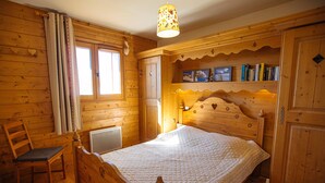 Une pièce en bois avec un lit, une chaise, un radiateur et une étagère remplie de livres.