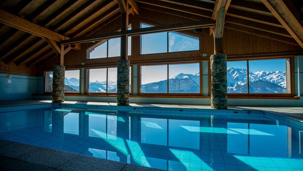 Une grande piscine intérieure offrant une vue dégagée sur les montagnes enneigées grâce à de larges baies vitrées.
