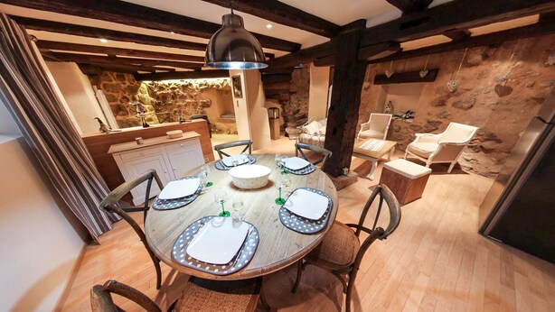 A dining area with a round table set for six, surrounded by chairs with a rustic design. - Gîte 'WINSTUB (Turckheim)