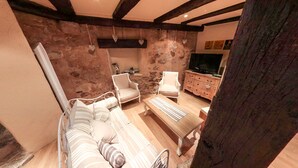 A cozy living room with a stone wall, a sofa, two armchairs, a wooden coffee table, and a TV stand. - Gîte 'WINSTUB (Turckheim)