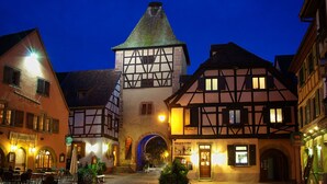 A traditional European town square with half-timbered buildings, a central tower, and outdoor seating areas. - Gîte 'WINSTUB (Turckheim)