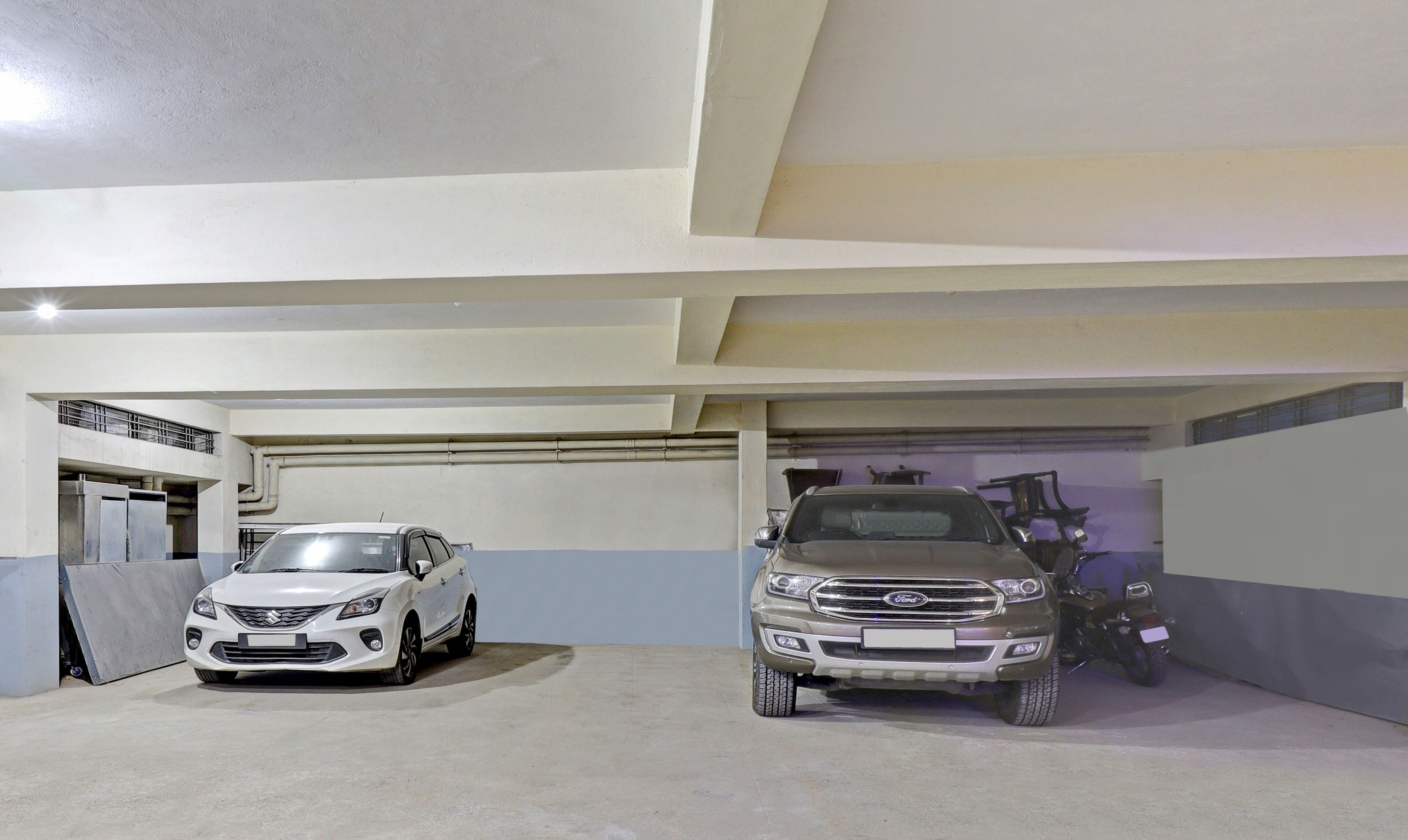 Een parkeergarage met twee geparkeerde auto's, één wit en één bruin, en een motorfiets op de achtergrond.