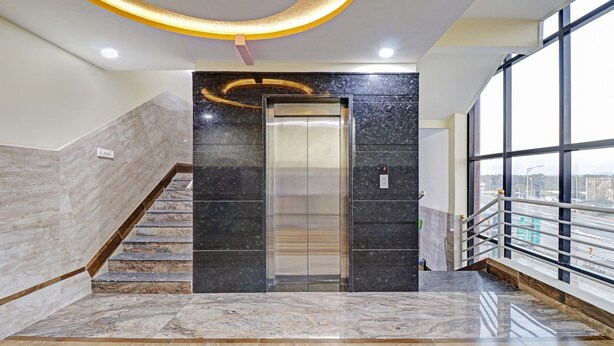Un ascensor moderno con pared de mármol, escalera de madera y barandilla de vidrio.