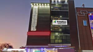 Un hotel moderno con un llamativo letrero de 'Treebo Skanda Suites', ventanas amplias y un elemento decorativo de luces verticales en la fachada.