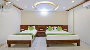 Habitación de hotel con dos camas, cabeceros de madera, ropa de cama blanca y una lámpara en el techo.