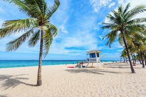Une plage bordée de palmiers, une tour de surveillance pour les sauveteurs, et l’océan en arrière-plan.