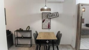 Un comedor con una mesa de madera y sillas negras, una estantería metálica y un letrero con la palabra 'SMILE' en la pared.