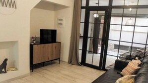Una sala moderna con un sofá negro, un mueble de madera y un televisor.