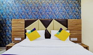 A hotel room with a patterned blue and white wall, a wooden headboard, and a bed with white bedding and two pillows. - Itsy Hotels Rk Palace (Vadodara)