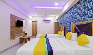 A hotel room with two beds, a TV mounted on the wall, a ceiling fan, and an air conditioning unit. - Itsy Hotels Rk Palace (Vadodara)