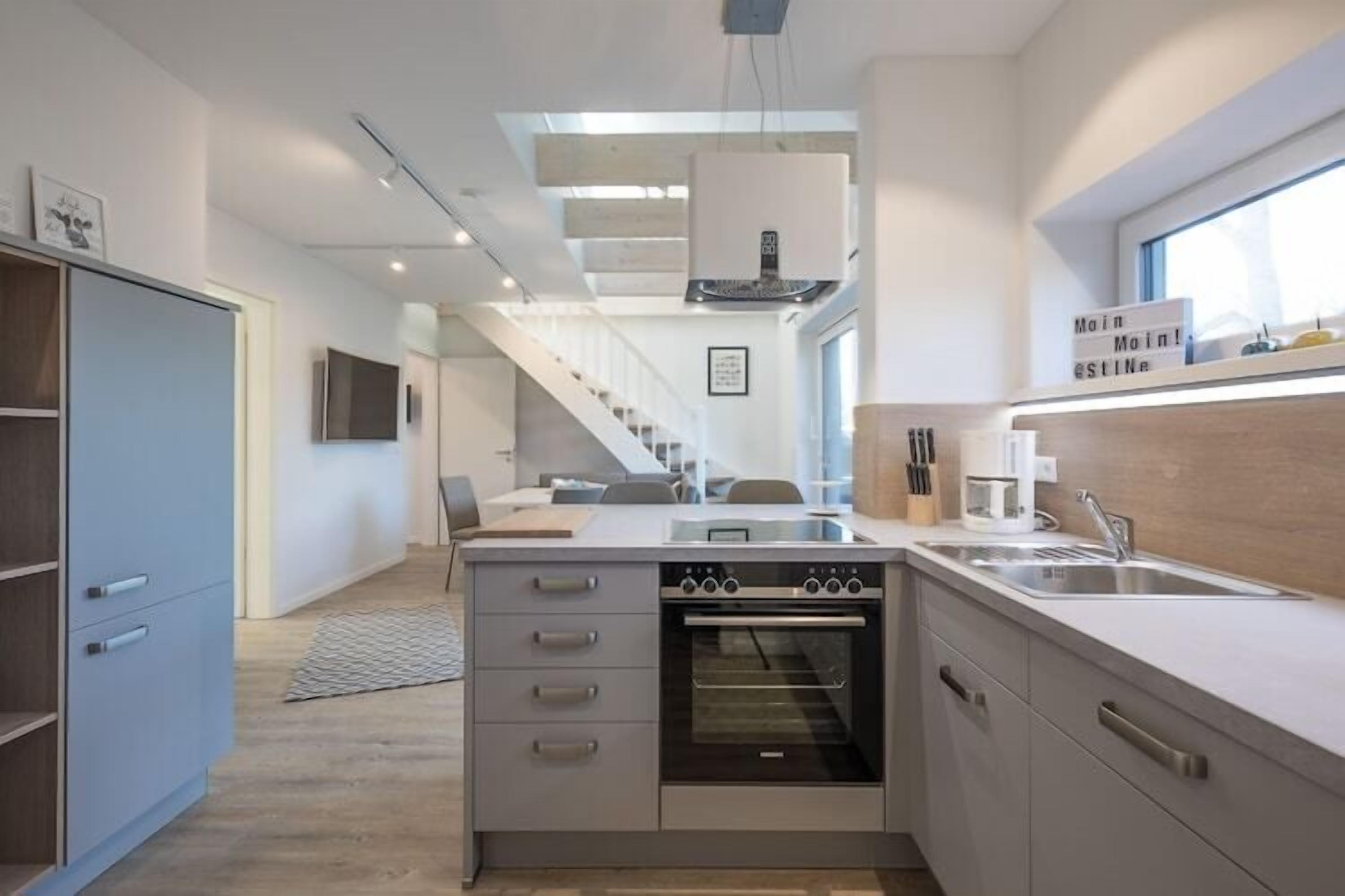 Una cocina moderna con horno integrado, una zona de comedor con mesa y sillas, y una escalera que sube a otro nivel.
